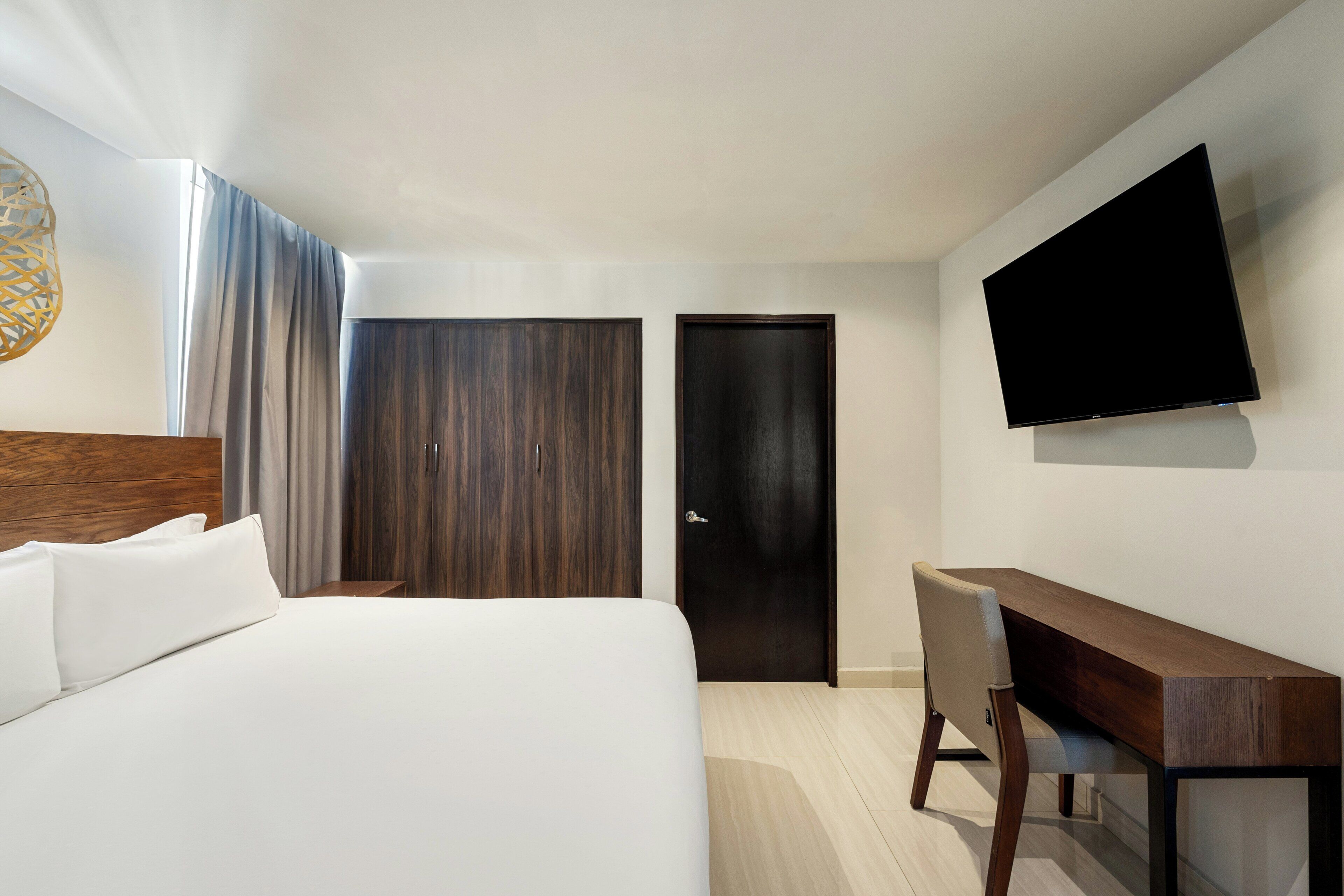 A hotel room with a bed, a desk, a chair, a TV, and two doors.