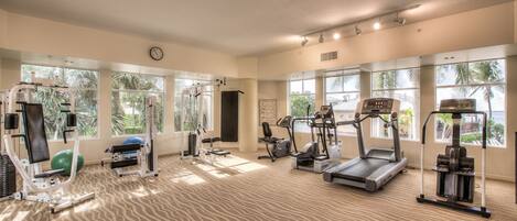 A gym with various exercise equipment, large windows, and a patterned carpet.