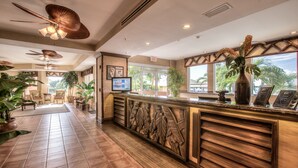 A hotel reception area with a wooden reception desk, ceiling fans, and large windows offering a view of palm trees. - Lovers Key Resort (Fort Myers Beach)