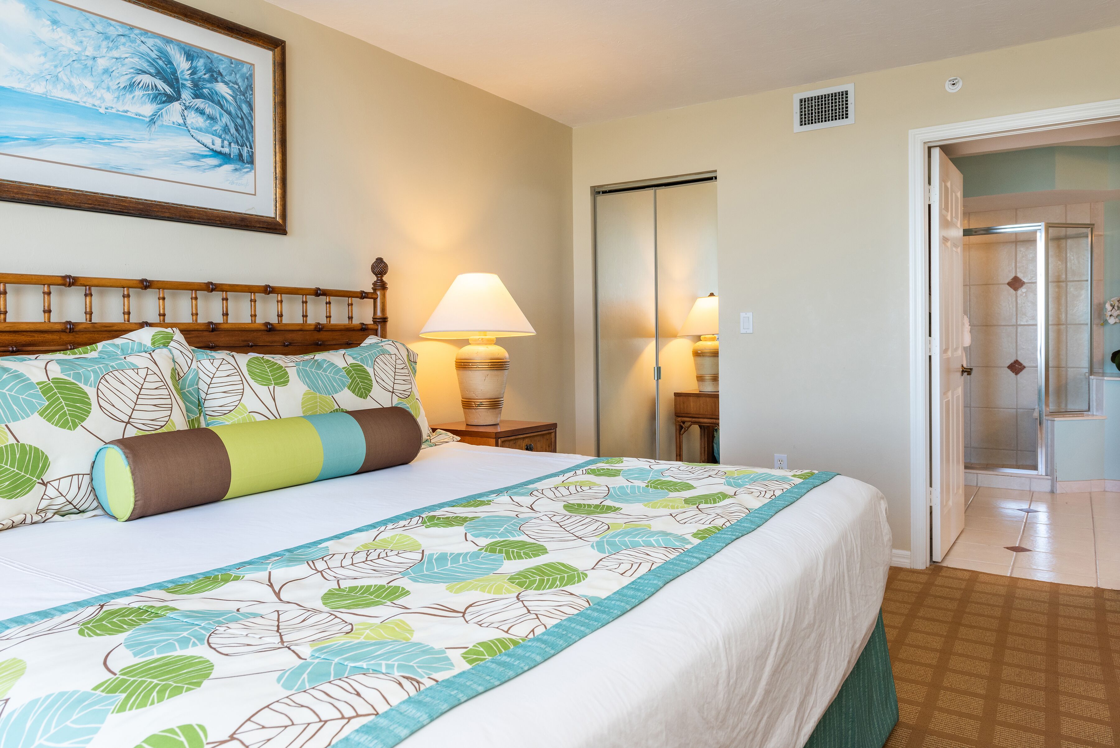 A hotel room with a bed, a nightstand, a lamp, a painting, and a bathroom door.