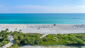 A beach with numerous umbrellas and lounge chairs, a lifeguard tower, and a road leading to the beach. - Hilton Vacation Club Crescent on South Beach Miami (Miami Beach)