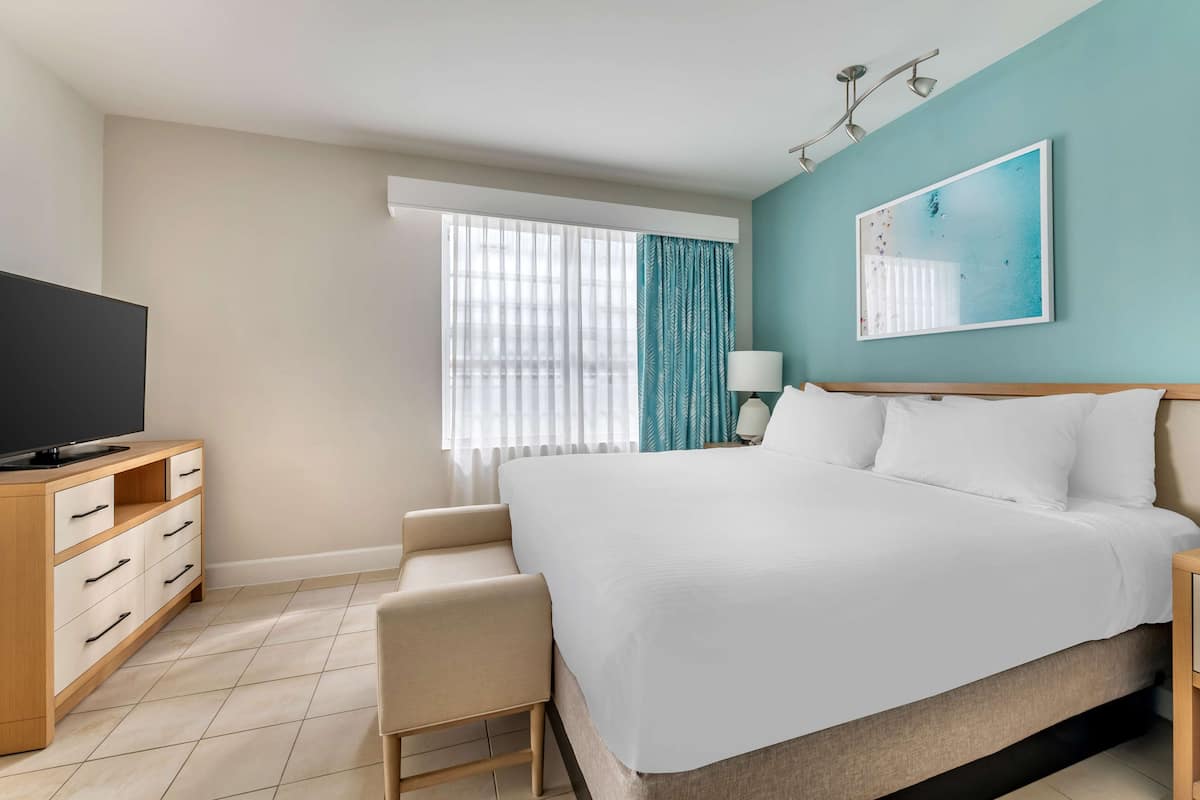 Une chambre d’hôtel avec un grand lit, une télévision, un bureau et une fenêtre avec des rideaux.