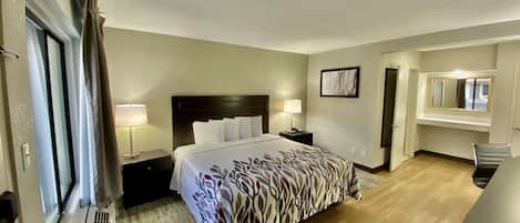 A hotel room with a bed, bedside tables, a desk, a chair, a window with curtains, and a door.
