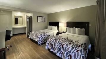A hotel room with two beds, a desk, a chair, a mirror, and a framed picture on the wall.