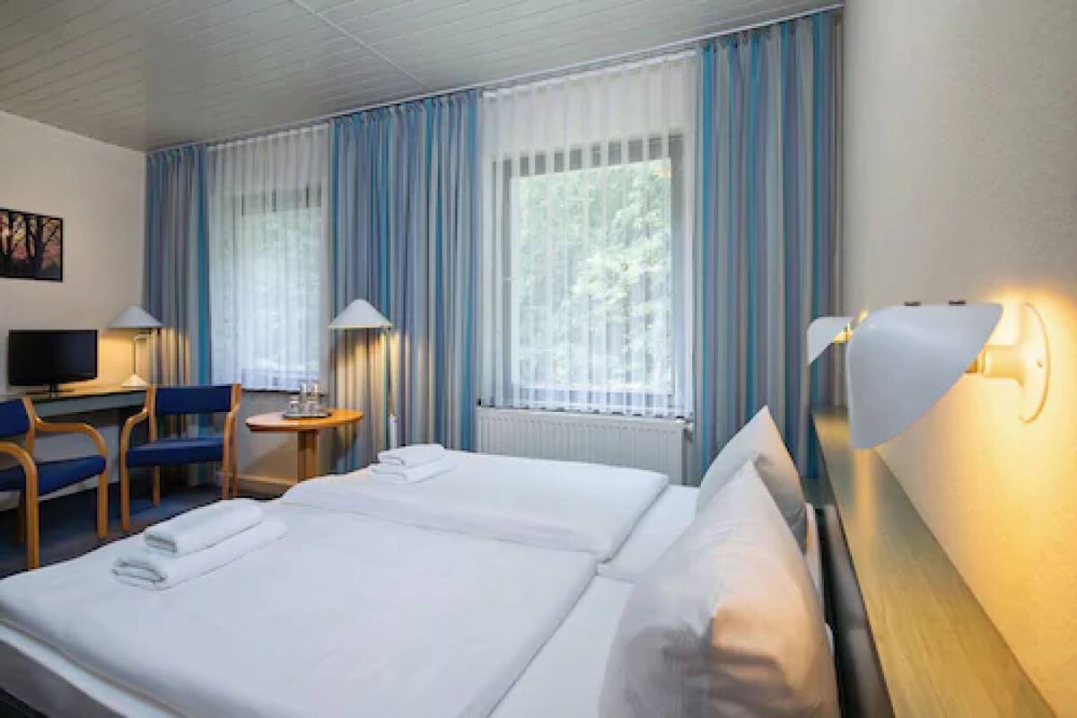 Habitación de hotel con dos camas, un escritorio con silla, televisión y lámparas.
