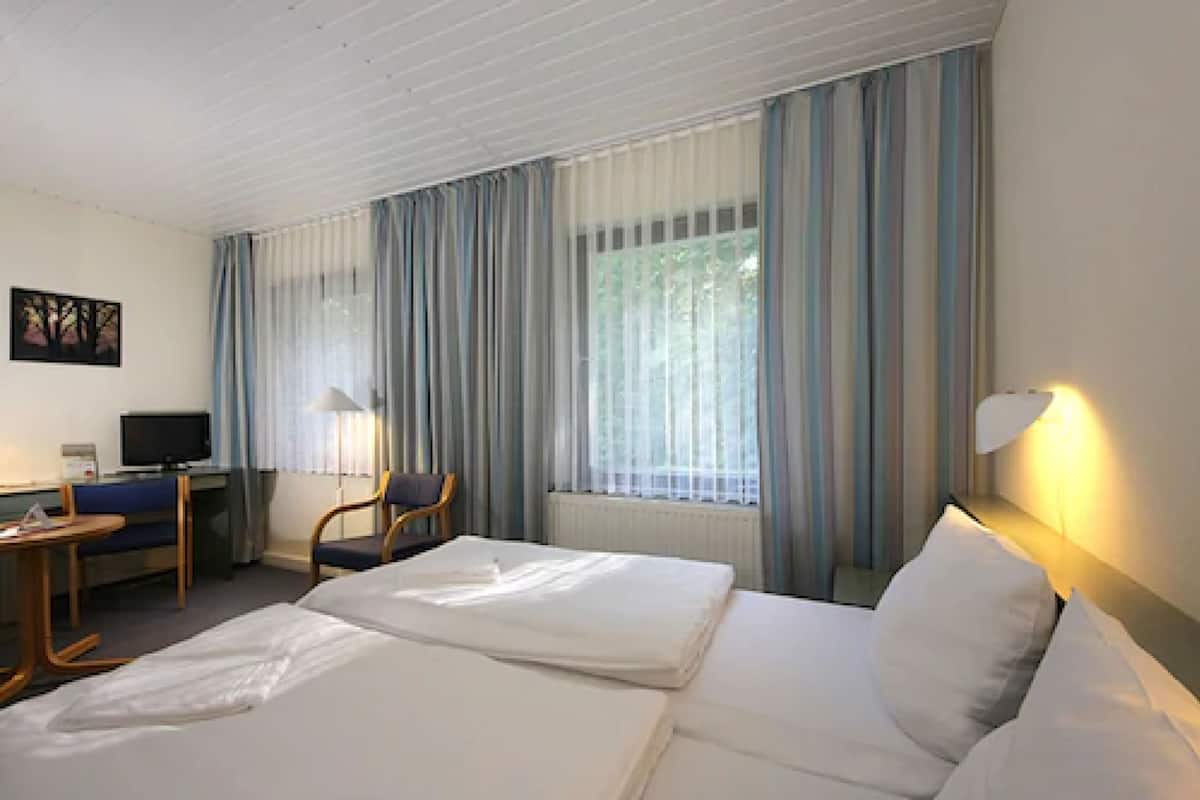 Una habitación de hotel con dos camas, un escritorio con una silla, un televisor y una ventana con cortinas.