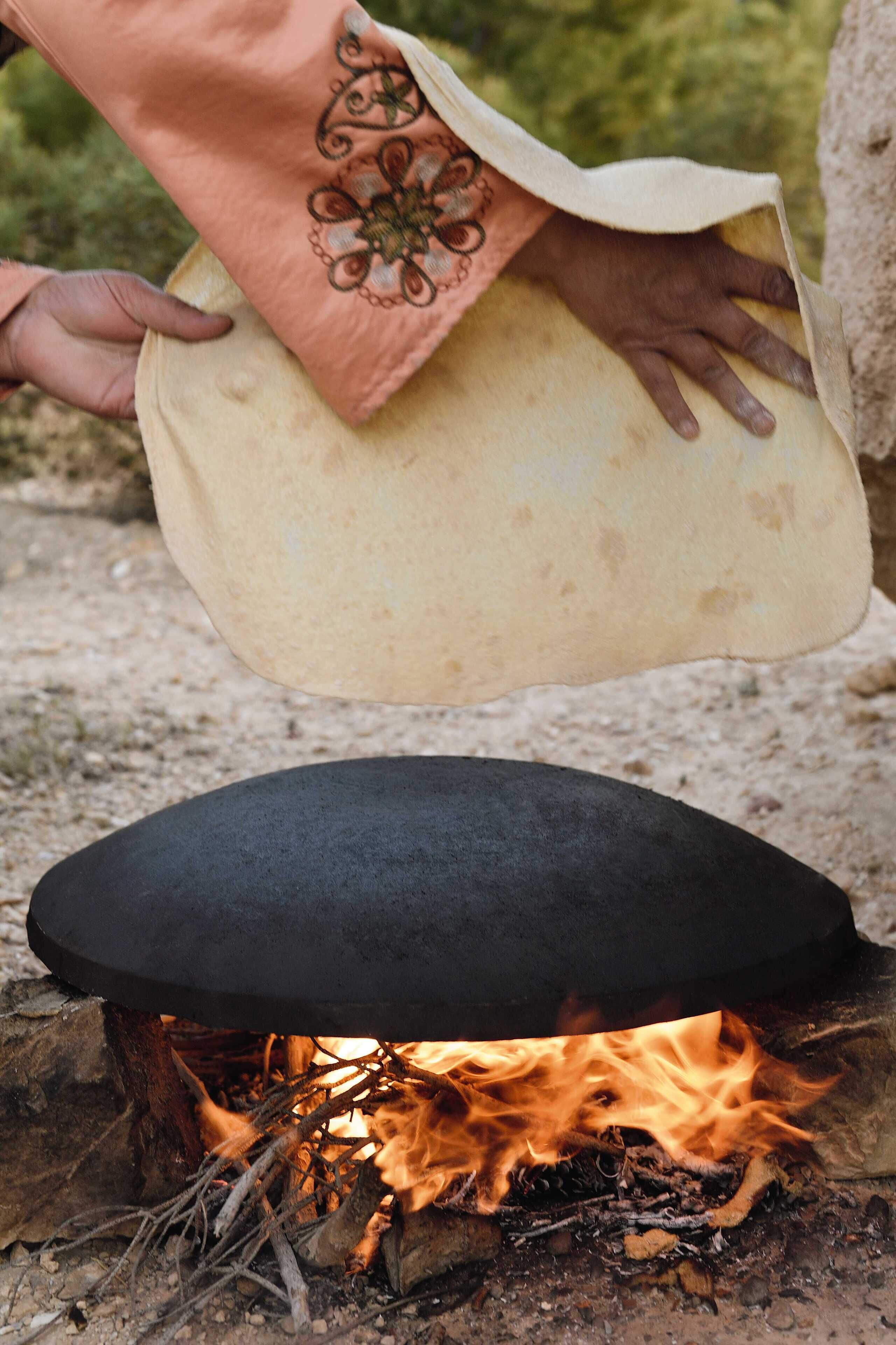 A person holding a flatbread over a fire.