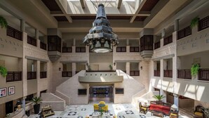 A spacious atrium with a central seating area, multiple balconies, and a decorative hanging light fixture. - Grand Mercure Petra (Wadi Musa)