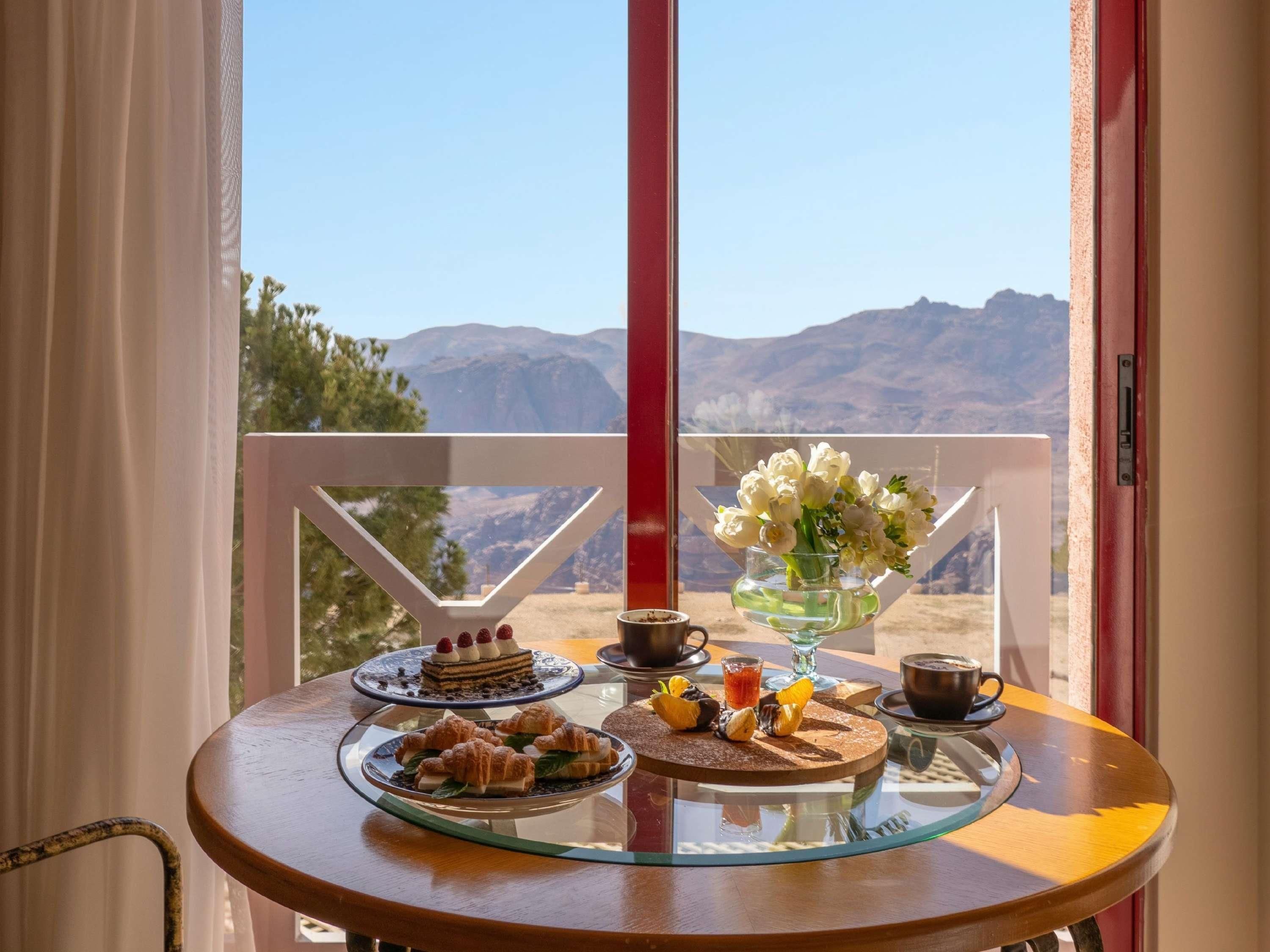 Una mesa con pasteles, un pastel y un florero, con vista a la montaña a través de una ventana.