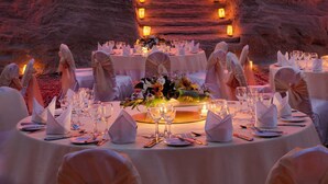 A formal dining setup with tables, chairs, and candles, set against a backdrop of ancient rock formations and a carved doorway. - Grand Mercure Petra (Wadi Musa)