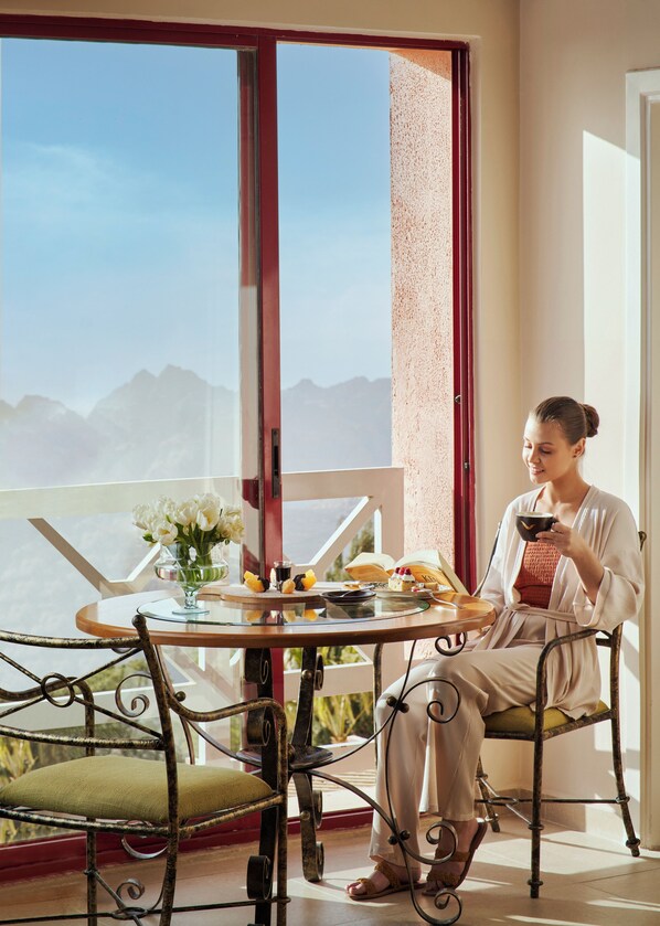 A person seated at a table with a view of mountains through a large window. - Grand Mercure Petra (Wadi Musa)