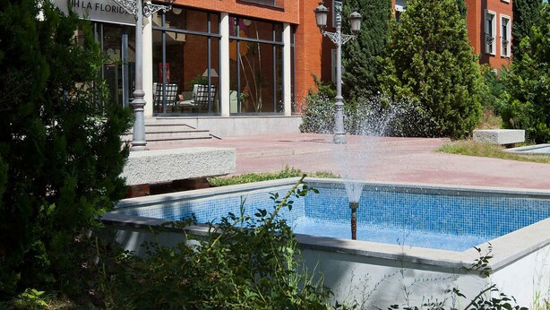 A building with a brick facade, large windows, and a fountain in front. - TH La Florida (Madrid)