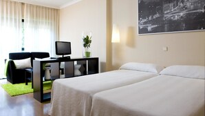 A hotel room with two beds, a desk with a television, a green plant, and a cityscape painting on the wall. - TH La Florida (Madrid)
