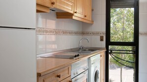 A kitchen with wooden cabinets, a stainless steel sink, a built-in oven, and a washing machine. - TH La Florida (Madrid)
