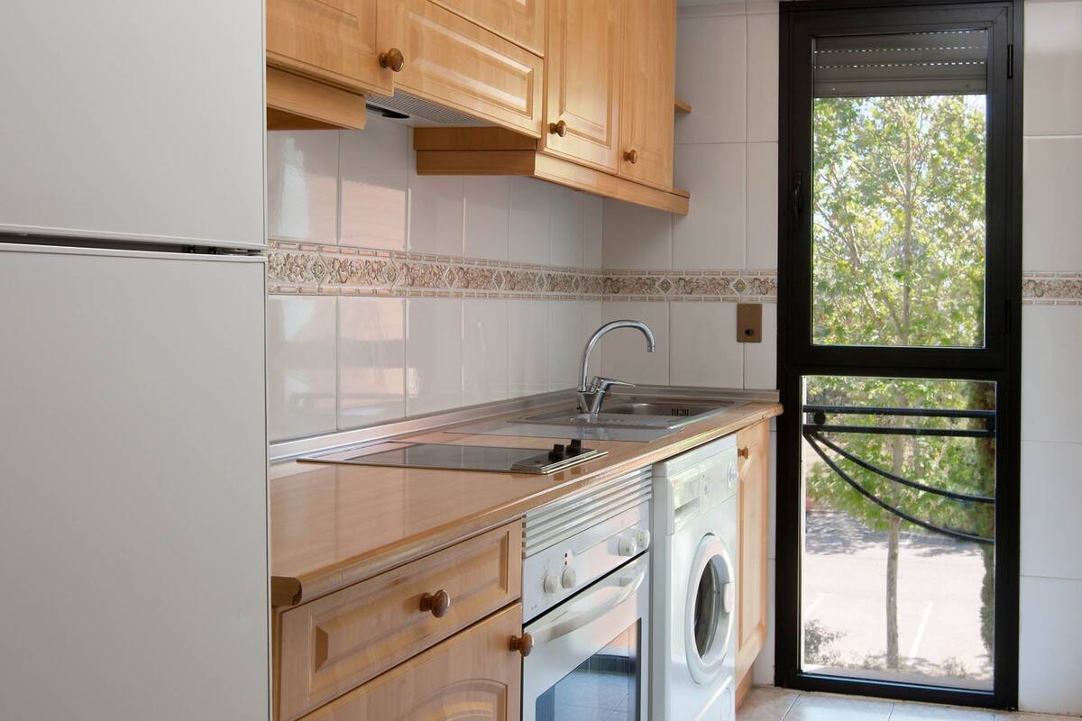 A kitchen with wooden cabinets, a stainless steel sink, a built-in oven, and a washing machine.
