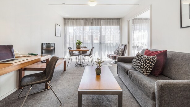 A modern living room with a wooden desk, a grey sofa, and a coffee table. - Punthill Little Bourke (Melbourne)
