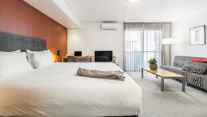 A hotel room with a large bed, a sofa, a desk with a computer, a TV, and a window with curtains. - Punthill Little Bourke (Melbourne)