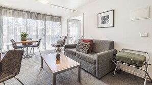 A modern living room with a grey sofa, a wooden coffee table, and a green suitcase on a metal stand. - Punthill Little Bourke (Melbourne)