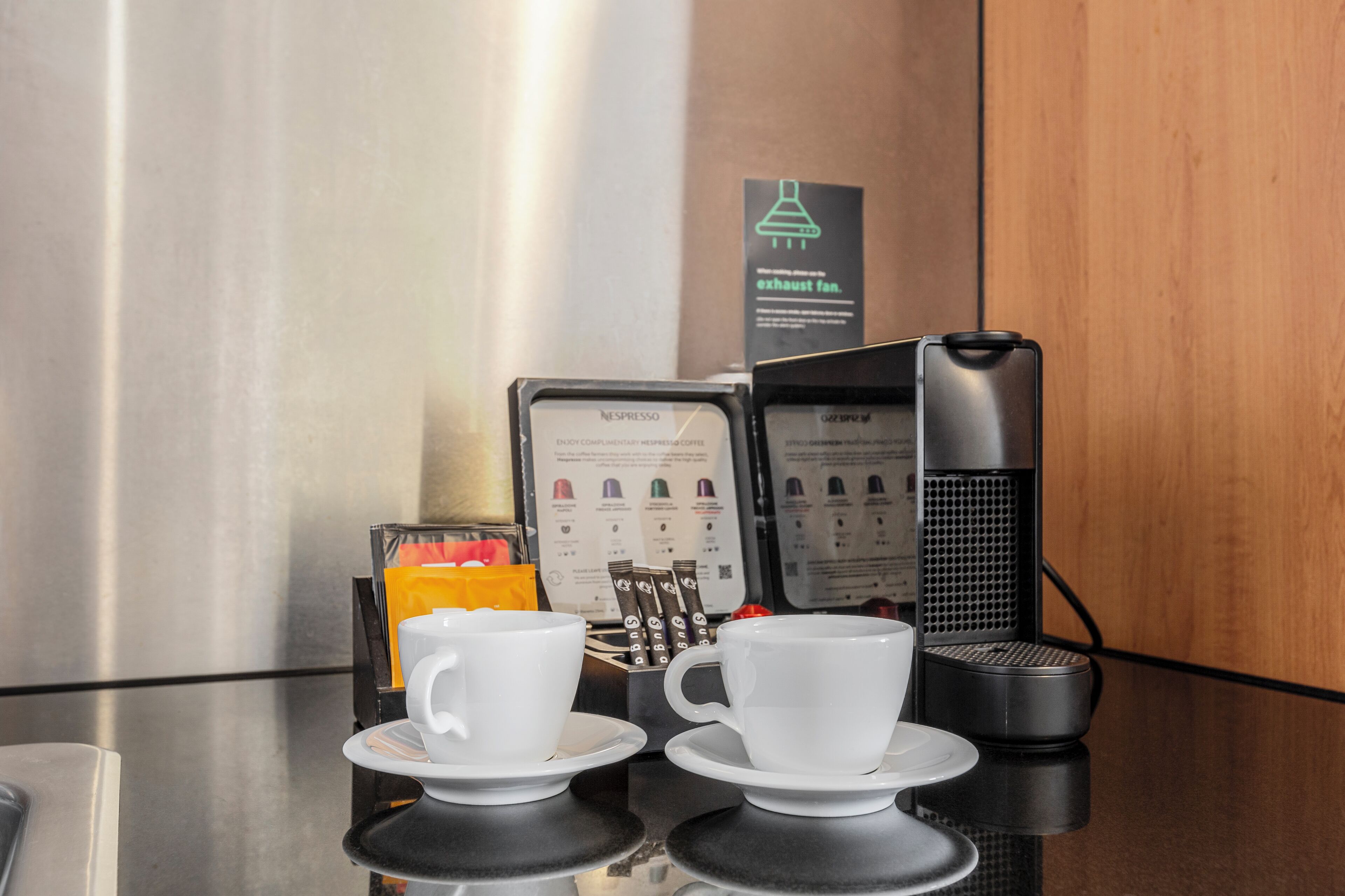 A coffee station with two white cups on saucers, a coffee machine, and a menu stand.
