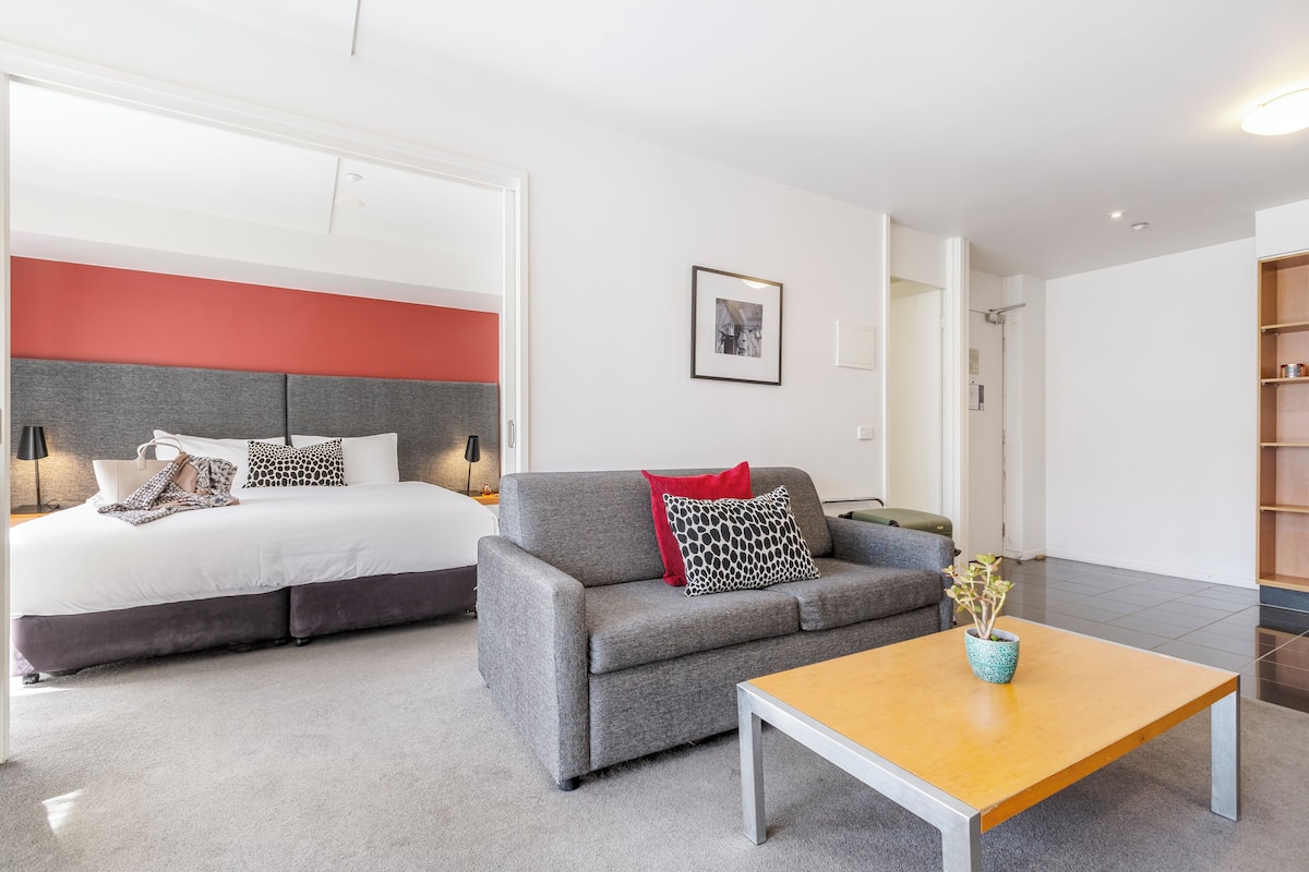 A modern bedroom with a bed, grey sofa, and a wooden coffee table.
