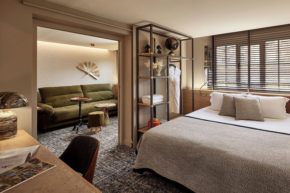 A modern hotel room with a bed, a sofa, a small table, and a walk-in closet.