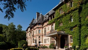 A historic building with a covered entrance, surrounded by lush greenery and a well-maintained garden. - Château Jeanne & the Forest - Château de Montvillargenne (Gouvieux)