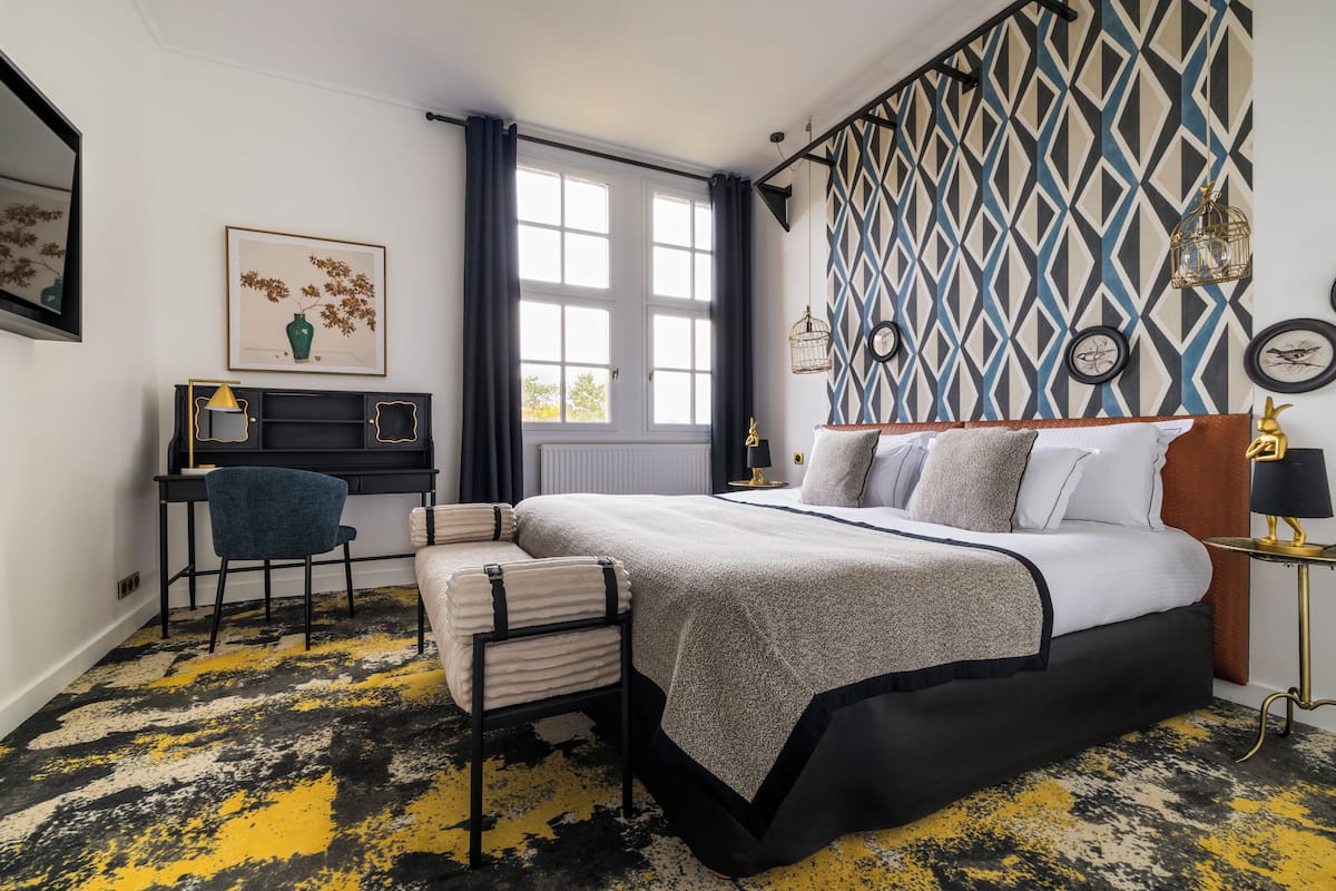 A modern bedroom with a bed, bedside table, lamp, and a desk with chair.