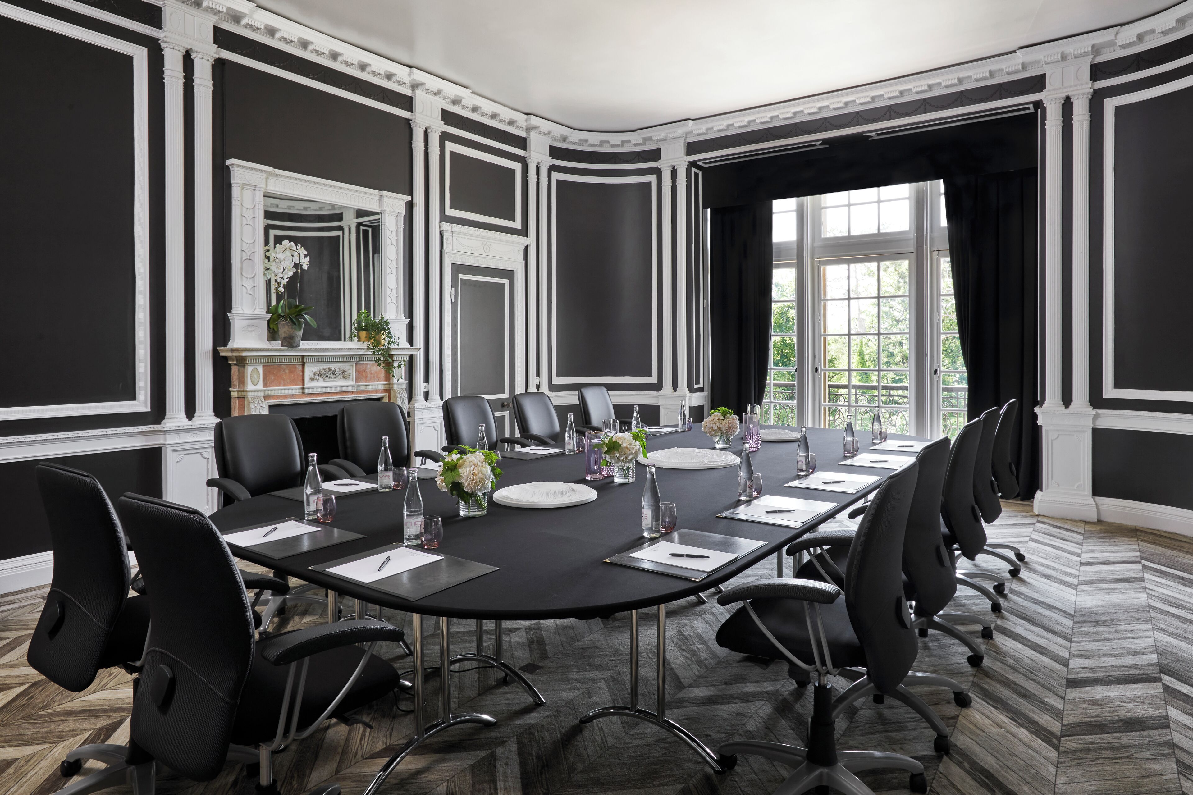 A conference room with a large oval table, black chairs, and a fireplace with a mirror above it.