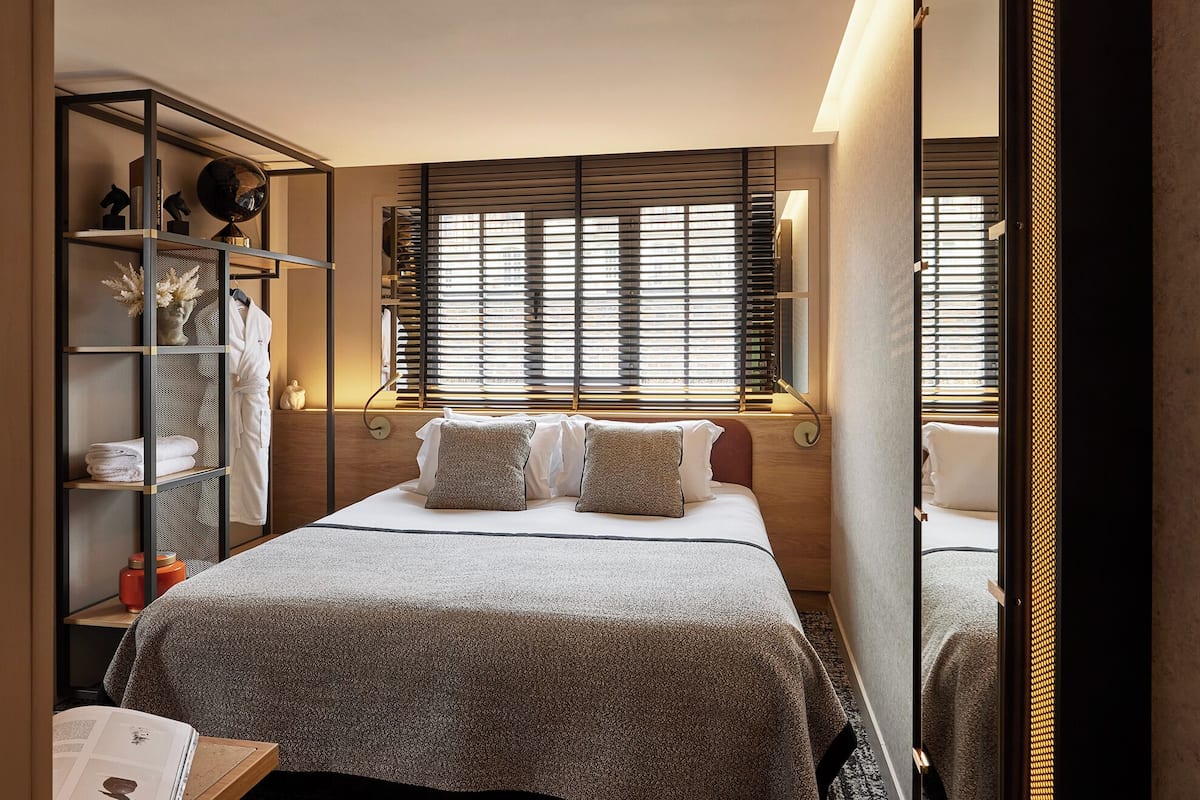 A modern bedroom with a large bed, a built-in wardrobe, and a window with blinds.