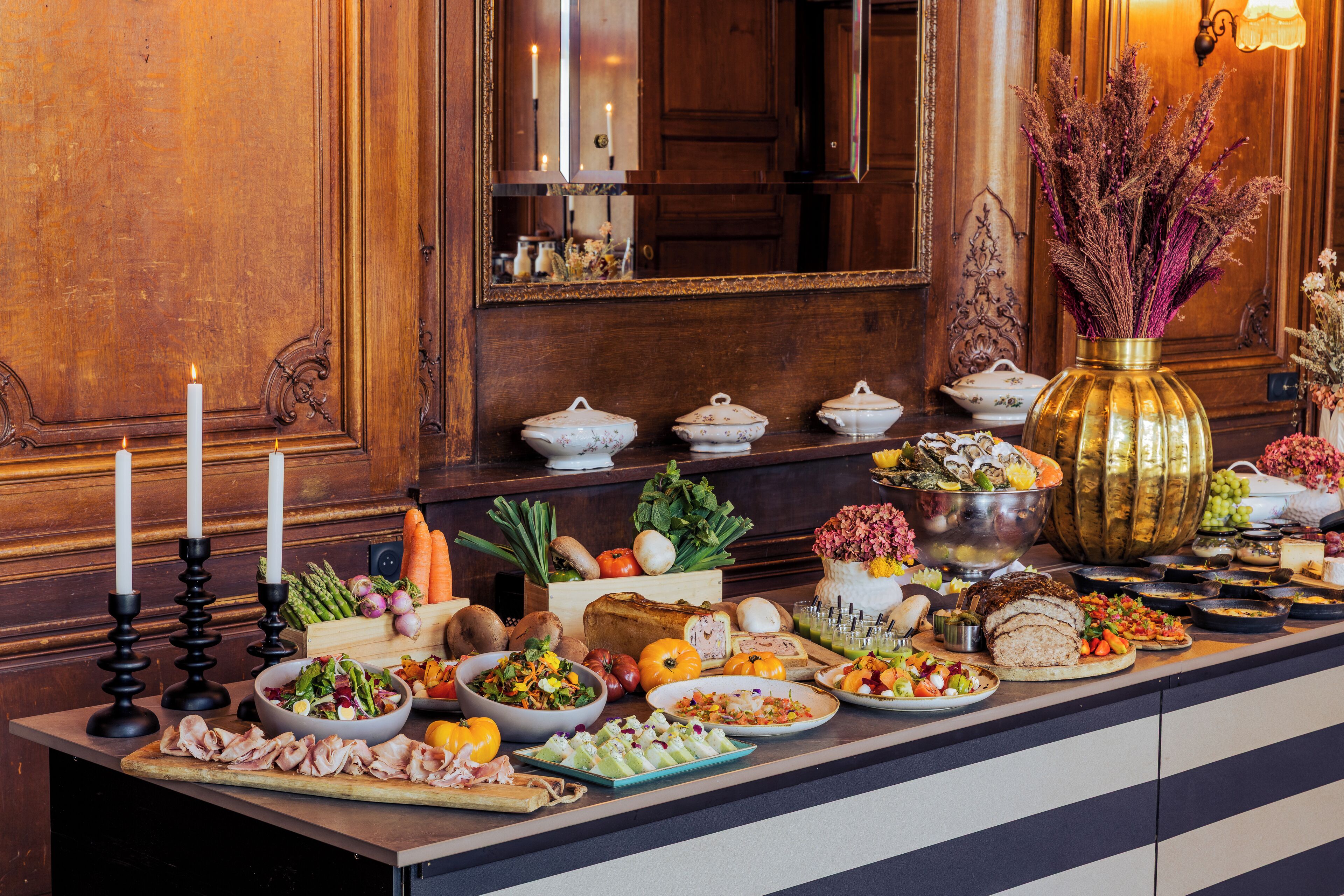 Una mesa de buffet con diversos platos y un gran jarrón de flores secas.