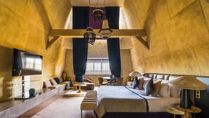 A high-ceilinged room with a large bed, a TV, and a dining area. - Château Jeanne & the Forest - Château de Montvillargenne (Gouvieux)