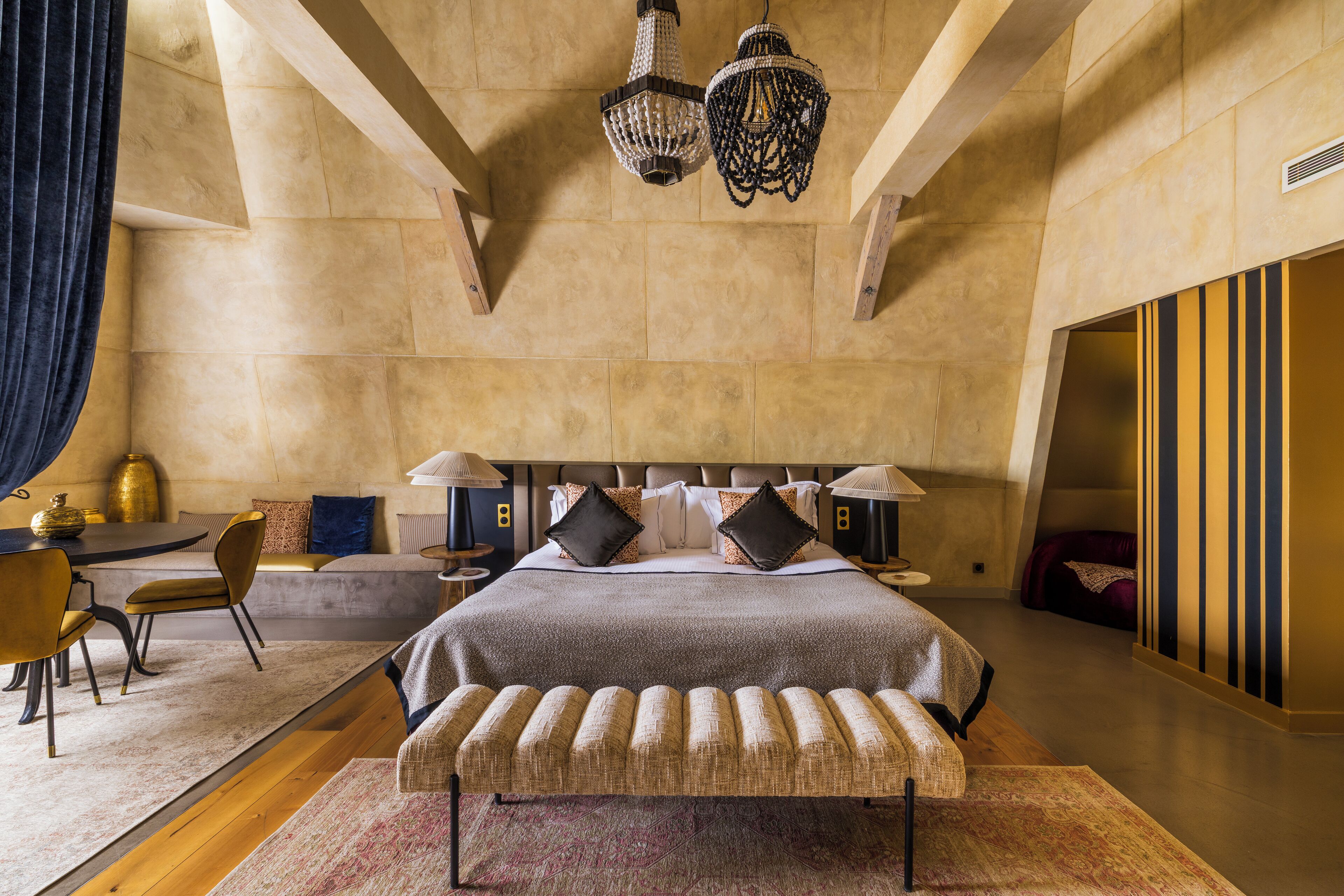 A spacious bedroom with a large bed, a bench, a desk, and two lamps.