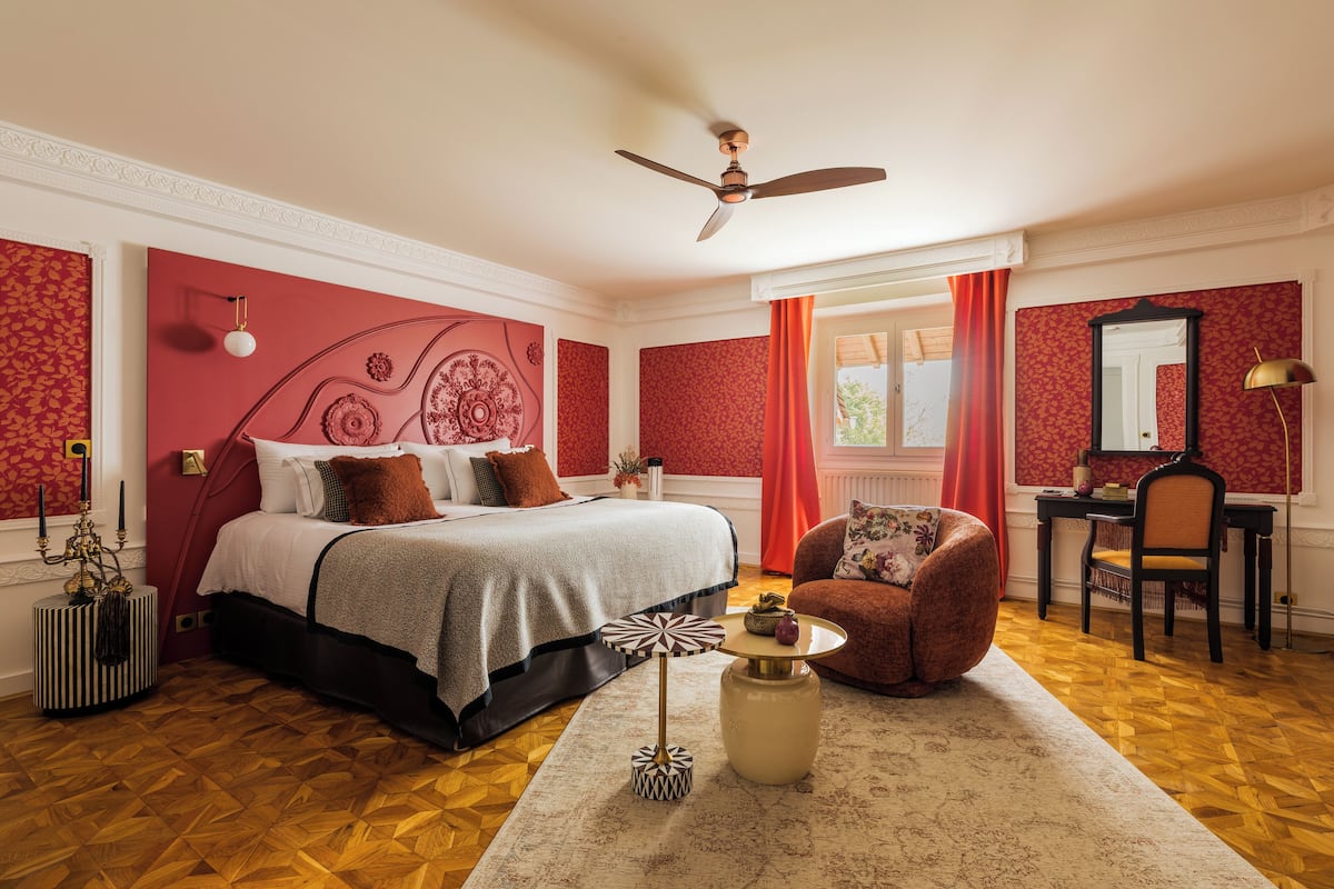 A bedroom with a bed, a desk, a chair, a ceiling fan, and a window with curtains.