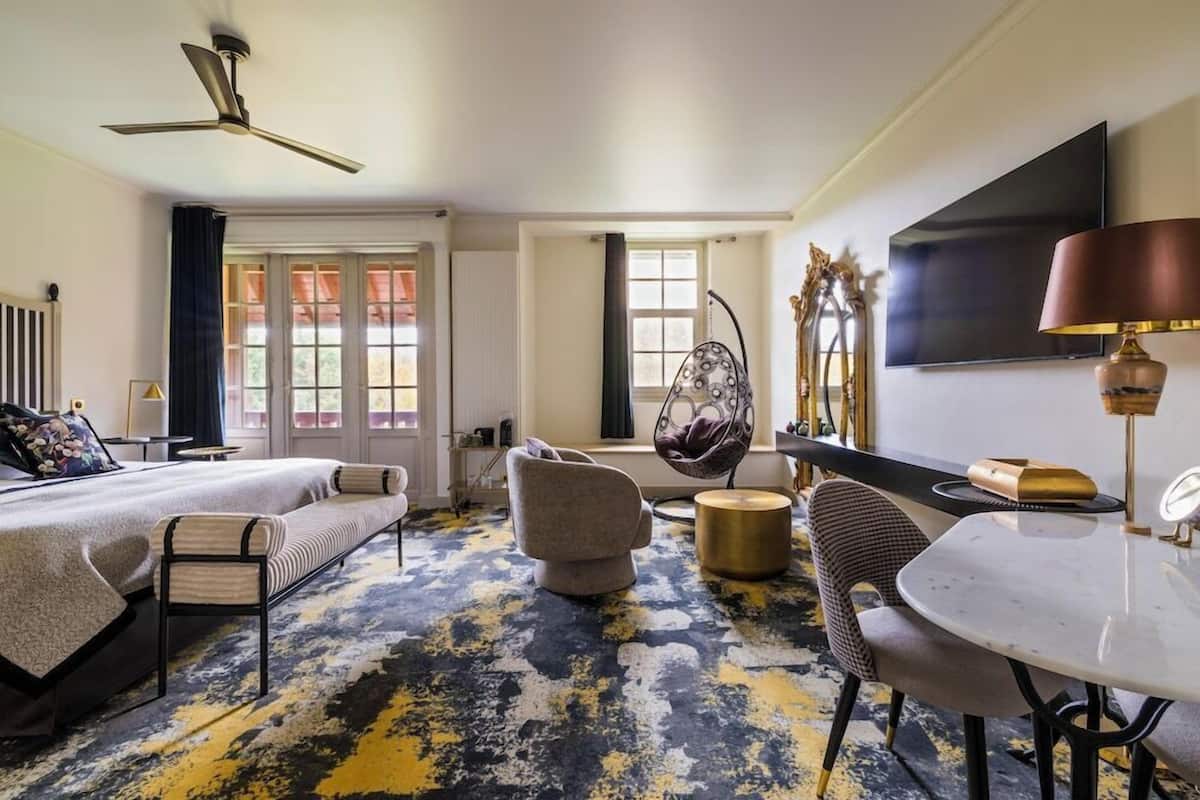 A hotel room with a bed, a sofa, a dining table, a hanging chair, and a TV.