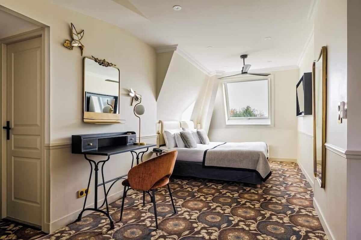 A bedroom with a bed, a desk, a chair, a mirror, and a window.