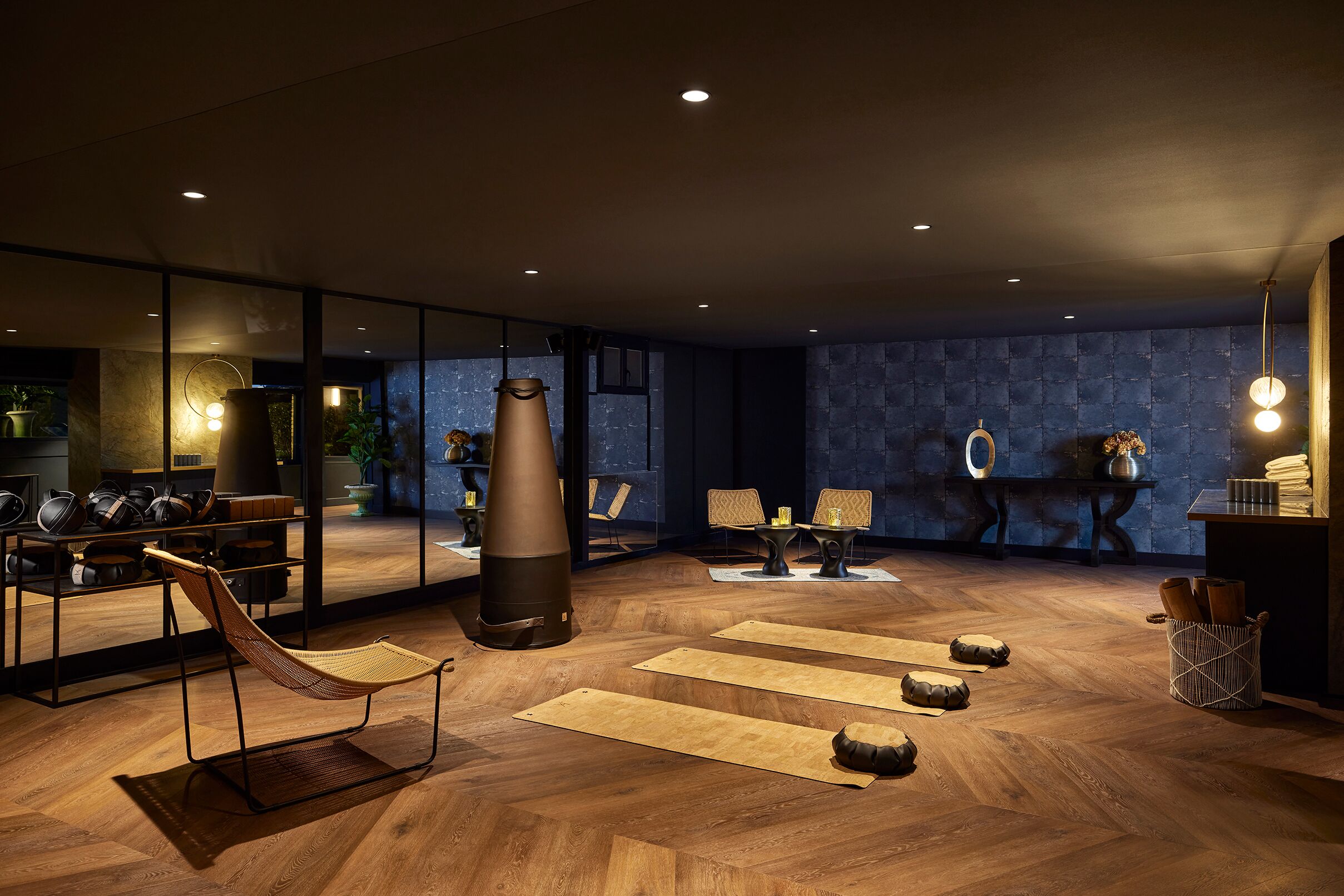 A modern interior with a wooden floor, a large mirror, and a seating area with a chair and cushions.