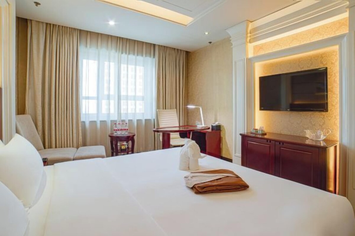 Une chambre d’hôtel avec un grand lit, un bureau, une chaise, un téléviseur fixé au mur et une fenêtre avec des rideaux.