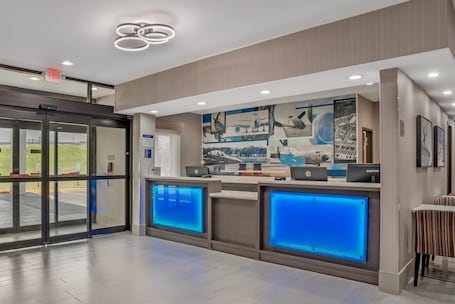 A reception area with a glass door entrance, a wall-mounted digital display, and a counter with a blue backlit panel.