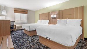 Ein Hotelzimmer mit zwei Betten, einem Schreibtisch, einem Stuhl, einem Fenster mit Jalousien und einem gemusterten Teppich.