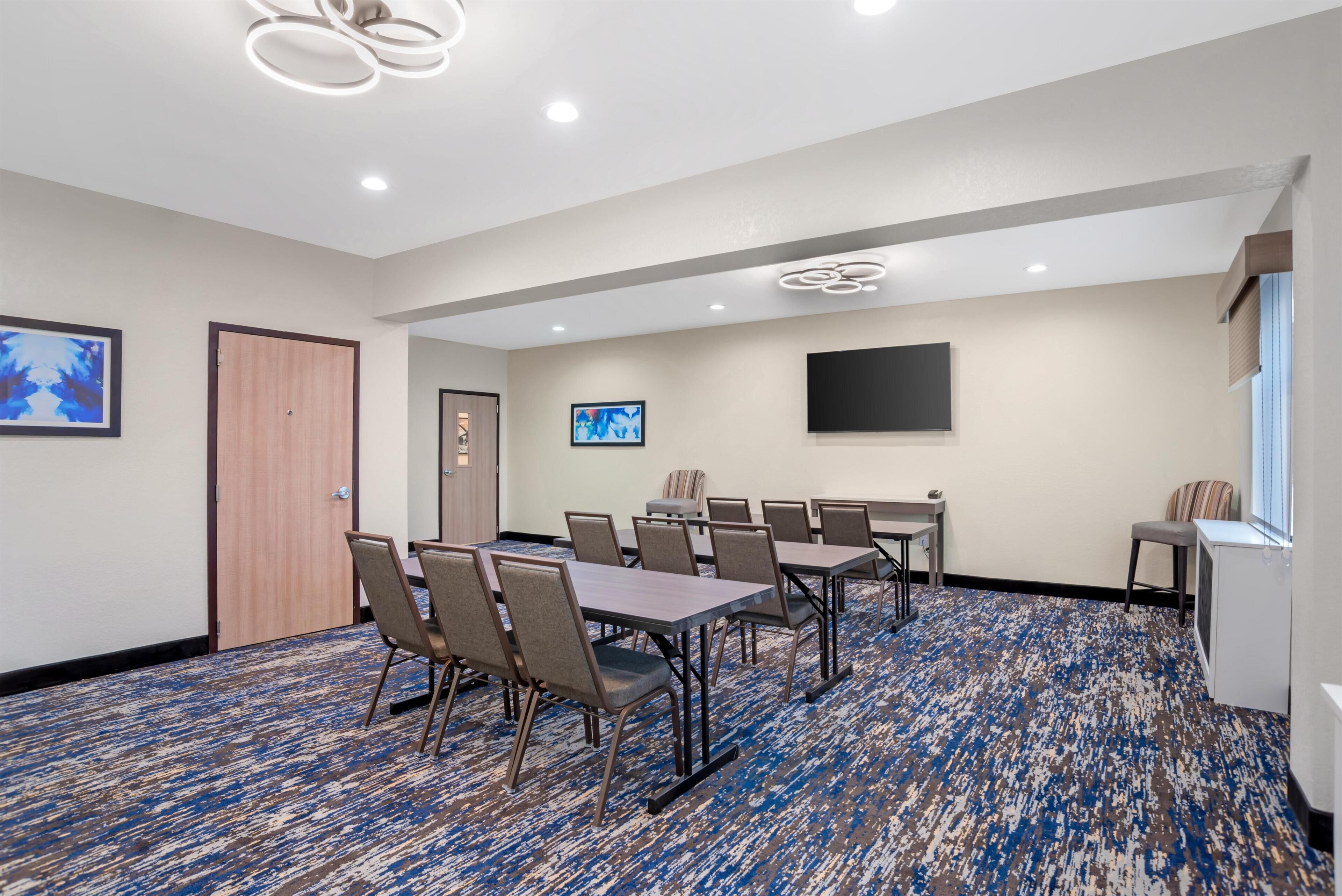 Une salle de conférence dotée d’un tapis à motifs, de tables, de chaises, d’un téléviseur à écran plat et d’œuvres d’art accrochées aux murs.