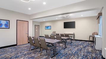 Une salle de conférence dotée d’un tapis à motifs, de tables, de chaises, d’un téléviseur à écran plat et d’œuvres d’art accrochées aux murs.