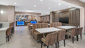 Eine moderne Hotelhalle mit Empfangstresen, Sitzbereichen und einem großen Fernsehbildschirm.