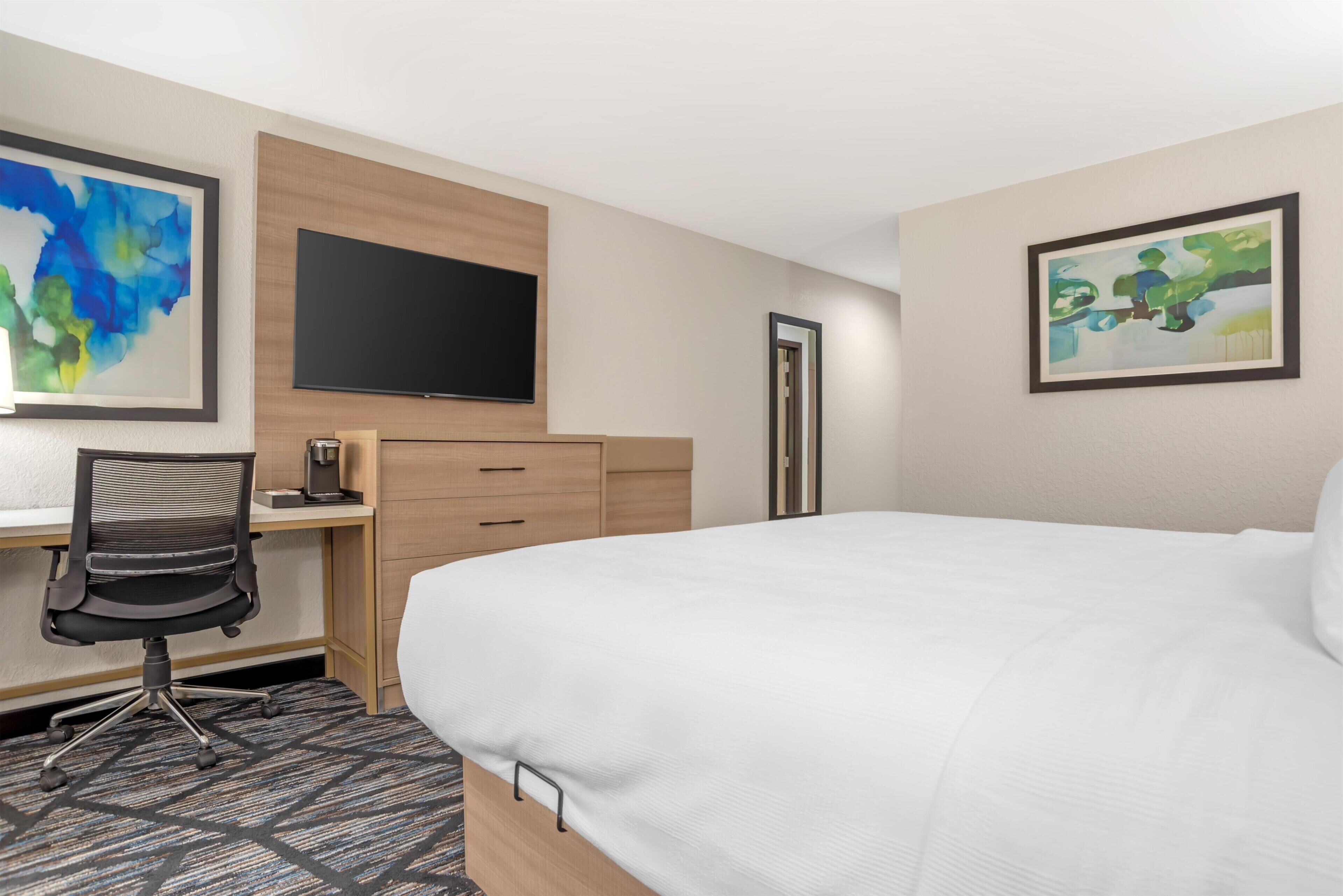 Ein Hotelzimmer mit Bett, Schreibtisch, Stuhl, Fernseher und Bildern an den Wänden.