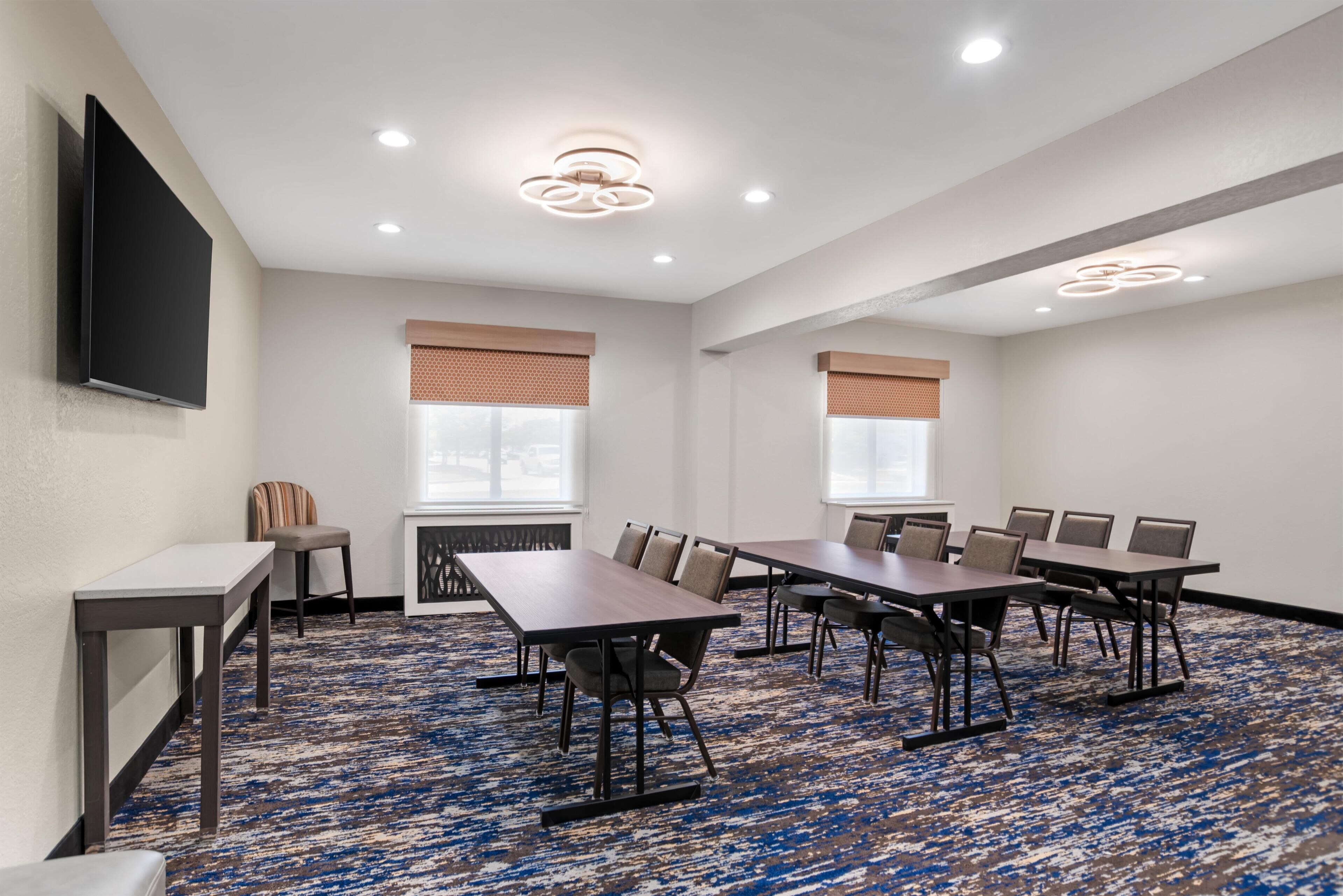A conference room with a large table, chairs, a flat-screen TV, and a patterned carpet.