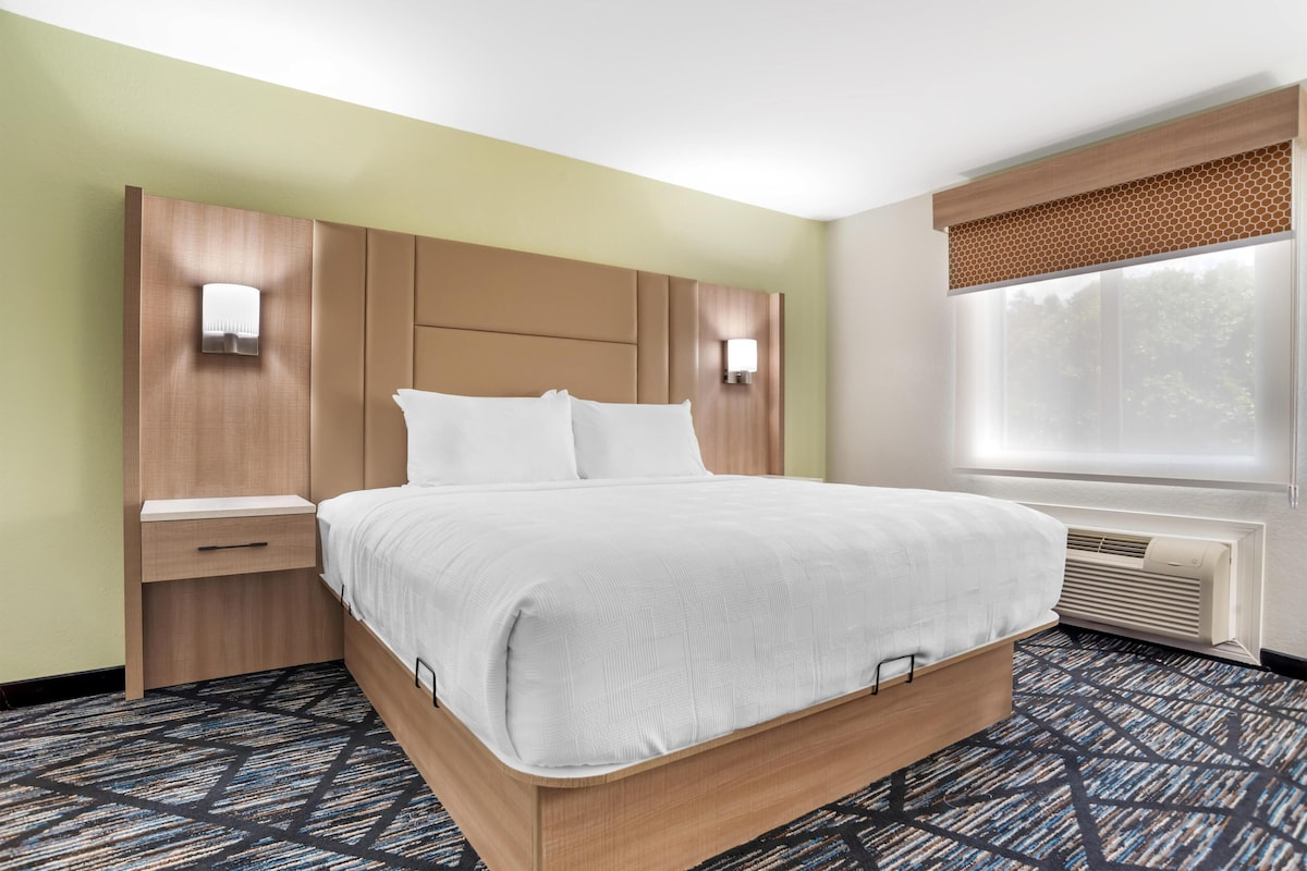Habitación de hotel con una cama grande, mesitas de noche, una ventana con persianas y un calentador fijado a la pared.
