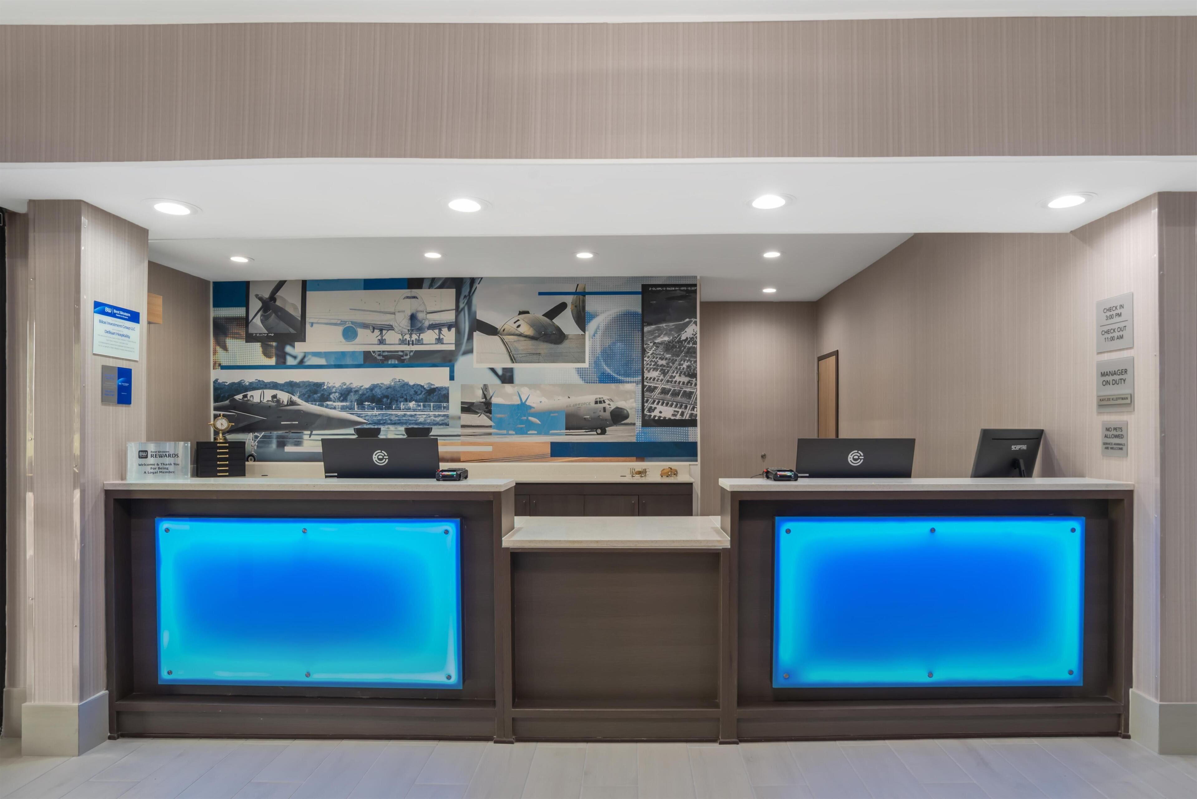 A reception desk with two computers, a blue-lit display, and a wall with aviation-themed artwork.
