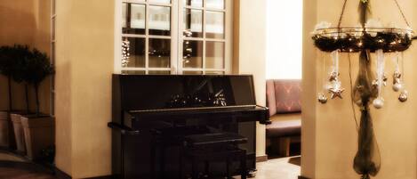 Un piano en una habitación cálidamente iluminada con un amplio ventanal arqueado, un banco y una lámpara de pie decorativa.