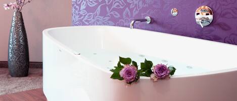 Un baño moderno con una bañera independiente, un florero con flores y un espejo decorativo.
