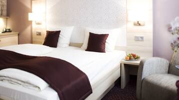 A hotel room with a large bed, a desk with a chair, a small table with a plate of fruit, and a decorative plant.