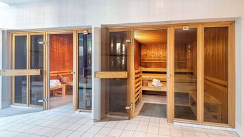 Zona de sauna con bancos de madera, algunos con toallas, y uno con una toalla y un vaso de agua.